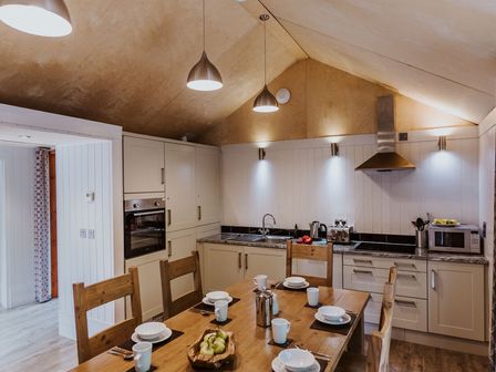 A kitchen with wooden chairs around a table set with white bowls and mugs at Lodge 8 in Corfe Castle