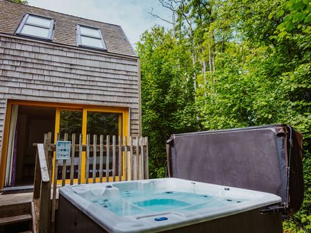 An outdoor hot tub next to a wooden house with sliding glass doors surrounded by trees at Lodge 17 in Corfe Castle