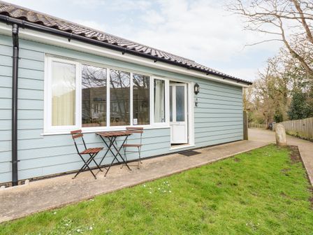 A blue exterior wall of a house with a white door and window and a small wooden table with two chairs on a concrete path at 10 The Dell in Mundesley