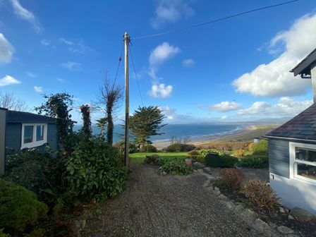 A garden pathway with bushes and trees leading to a view of a sandy beach and the sea with houses on either side at Sibrwd Y Mor in Harlech
