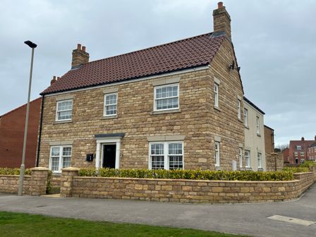 A two story stone house with a tiled roof and surrounding low stone wall and greenery at High Mill House in Scalby