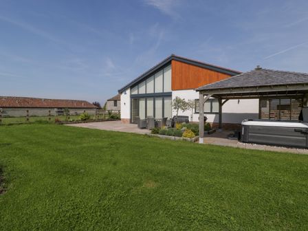 A backyard with green lawn a wooden pergola with a hot tub patio furniture and a modern house at Bilsham Meadows in Aust