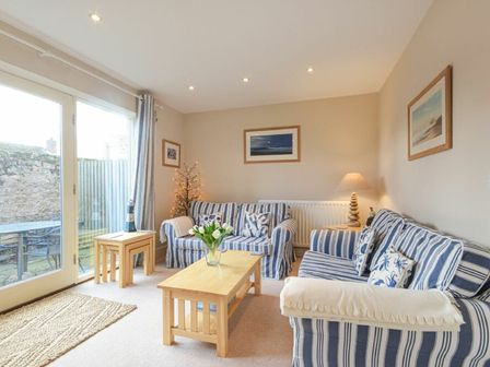 A living room with striped sofas coffee table and sliding glass doors at Smugglers Cove 7 in Beadnell