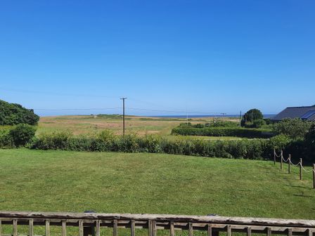 A grassy lawn with hedges and utility poles overlooking fields and a distant view of the sea at Timbers in Weybourne
