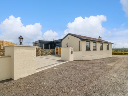 Exterior view of a single-story house with a gravel driveway and stone wall at Refail Fach Near Cemaes Bay