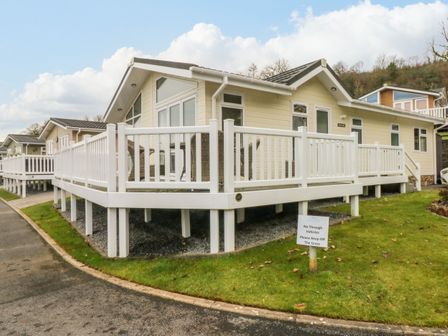 A beige lodge with white railings on a raised deck and grass around at Dono's Lodge Stepaside near Kilgetty Heritage Park