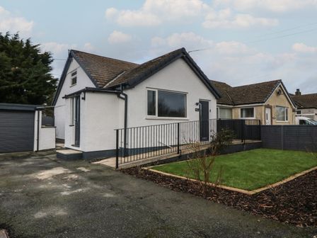 A white house with a tiled roof and a ramp leading to the front door next to a small lawn at Ty Nain in Llanfairpwllgwyngyll