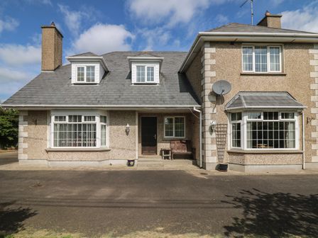 The exterior front view of a two-story house with two bay windows a wooden bench and paved driveway at Bolger House in Ballintubbrid near Kilmuckridge County Wexford