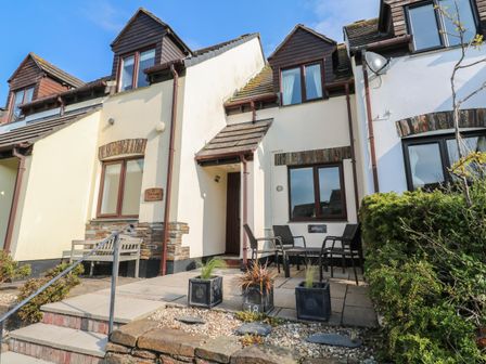 Exterior of a cottage with a small patio table and chairs and a bench at Bumbles in Padstow
