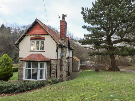 A two-story stone and plaster house with a tiled roof surrounded by grass trees and shrubs at Butlers Cottage in Cloughton near Scarborough