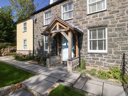 Stone house exterior with wooden porch and blue door at Belle View in Llaniestyn near Abersoch