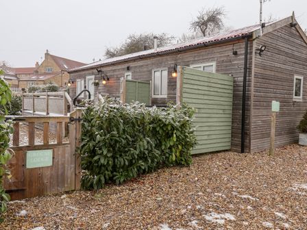 A wooden lodge with a gravel driveway bushes and wooden gates at Grouse Lodge in Seamer North Yorkshire