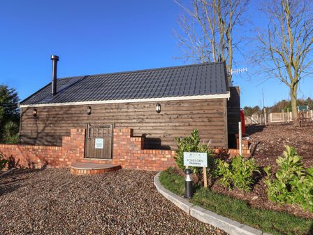 A wooden cabin with a tiled roof and brick wall surrounded by gravel and plants at Foxes Den in Seamer North Yorkshire