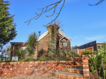 Exterior view of a wooden cabin with a tree stump in front and brick steps leading up to it at Sunset Retreat in Seamer North Yorkshire
