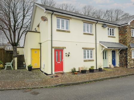 A row of townhouses with red green and blue doors and potted plants on the sidewalk at 1 Bethany Court in Bodmin