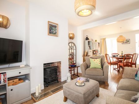 A living room with a TV cabinet, armchair, ottoman, fireplace, and dining table with chairs at Quarrier's Rest in Swanage