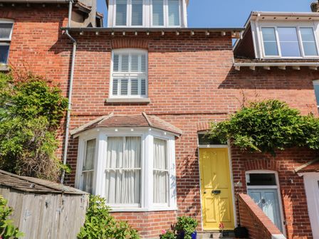 A brick house exterior with a yellow door and white bay window surrounded by greenery at Mayflower 9 Coronation Road Salcombe