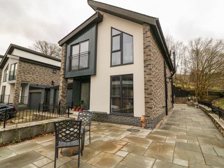 A modern house exterior with patio chairs and a paved walkway at Ty Bains in Llanberis