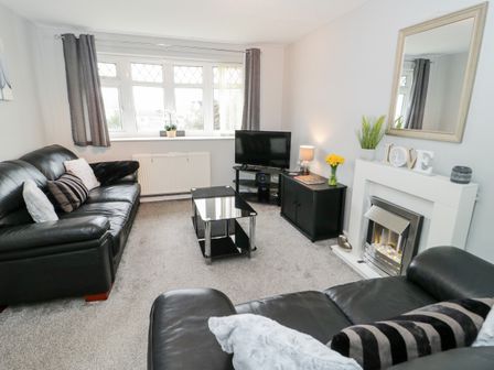A living room with black leather sofas a glass coffee table and a fireplace at 17 Ffordd Gwenllian in Llanfairpwllgwyngyll