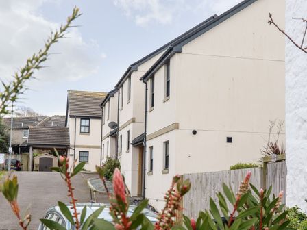 A residential area with cream-colored houses a driveway and plants in the foreground at 1 Queensway Gardens in Hayle