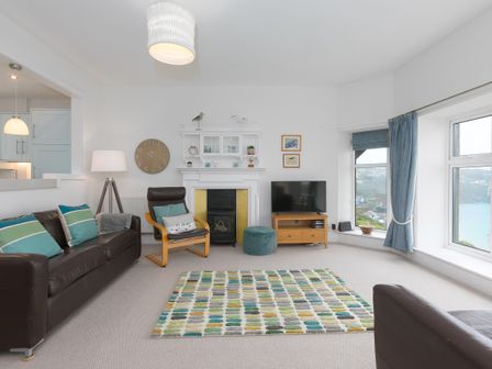 A living room with a brown leather sofa and armchair a fireplace a television and large windows with blue curtains at 4 Pentowan Court in Carbis Bay