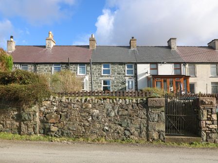A row of stone houses with a stone wall and metal gate in front at Bod Feurig in Penygroes