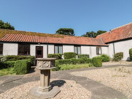 A courtyard with trimmed bushes and a stone pedestal in front of a building with a tiled roof at Highcliffe Cottage in Flamborough