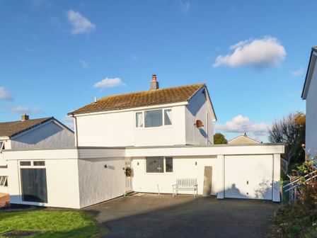 A two-story house with a garage and driveway under a blue sky at Artro in Cemaes Bay