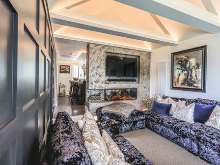 A living room with a sectional sofa and pillows a fireplace with a mounted TV and a painting on the wall at Whisk Away Cottage in Greystoke near Troutbeck Near Penrith