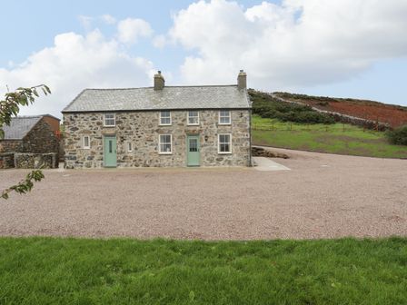 A stone house with green doors and windows on a gravel area with grassy hill behind at Pennant Igyn in Mynytho near Abersoch