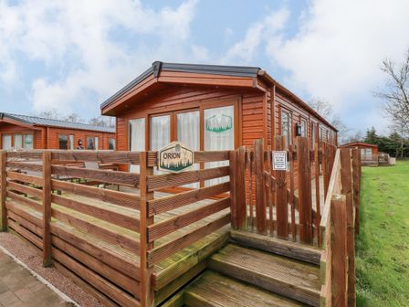 A wooden cabin with a fenced deck and steps leading to the entrance at Orion in Felmoor Park