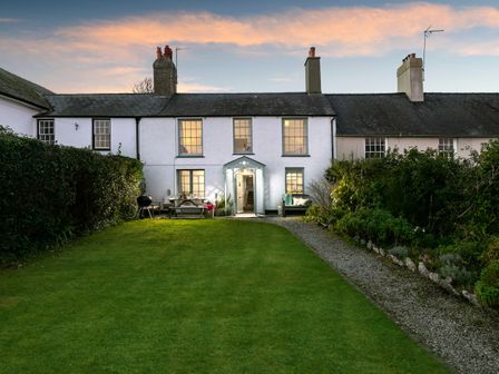 A grassy backyard with a gravel path leading to a white two-story house with lit windows at Tros Yr Afon in Beaumaris