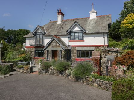 A stone and white house with a small balcony and garden in front at Storrs Lodge in Bowness-On-Windermere