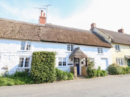 A thatched roof cottage with white walls green bushes and a blue door at Lime Cottage in Burton Bradstock