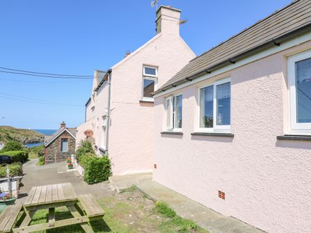 The exterior of pink textured houses with white window frames and a wooden picnic table on grass near the coast at 2 Sunny Hill in Porthgain near St Davids