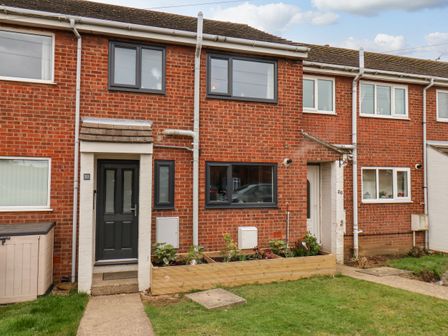 A brick terraced house with black framed windows and a black door with a small garden bed in front at 22 Constable Road Hunmanby