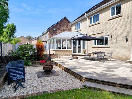 A backyard with a patio table and chairs under an umbrella a fire pit with benches on a gravel area and a conservatory at Sanderson House in Cleator Moor