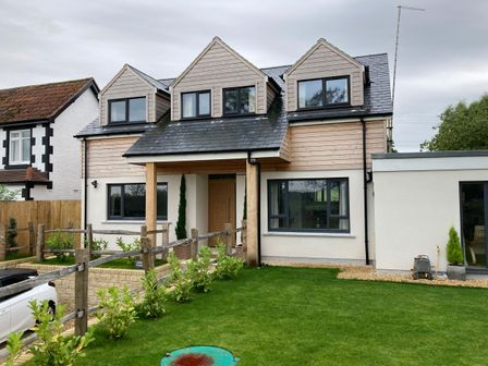 Front view of a two-story house with three dormer windows a wooden fence and a green lawn at Little Foxes in Studley near Calne