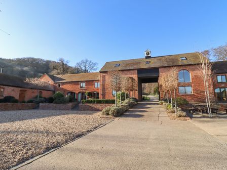A brick courtyard with trimmed trees and a clock tower at the top of a large building at Fairoaks Barns in Hollybush near Ledbury