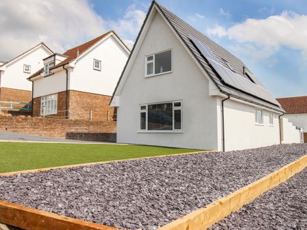 A white house with solar panels on the roof a lawn and a gravel garden at The White House in Weymouth