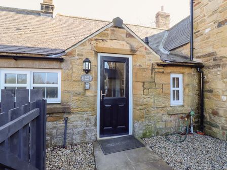 Stone exterior of a cottage with a black door and two windows with white frames at Ash Cottage in Lucker near Warenford