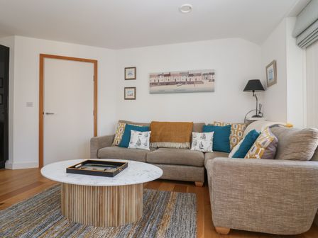 A living room with a beige sofa, a round wooden coffee table, wall art, and a lamp at Skylark in Southwold