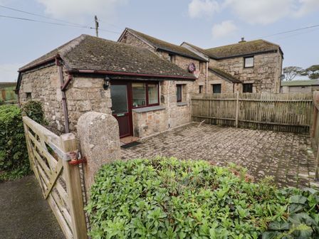 A stone building with a gated entrance and a paved courtyard surrounded by a wooden fence at Ramblers Rest in St Just
