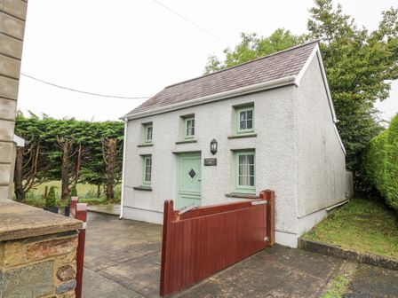 A white house with green windows and door behind a wooden gate at Ty Bach Twt in Synod Inn near New Quay