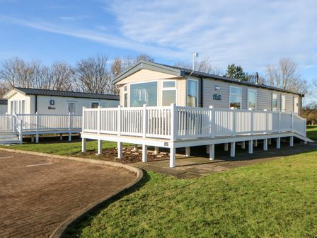 A mobile home with a wraparound white railing deck on grass at 17 Summer Meadows in Ashington