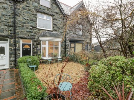 A stone house exterior with a black door and bay window with metal chairs and a gravel garden at Bronwen House in Llanbedr