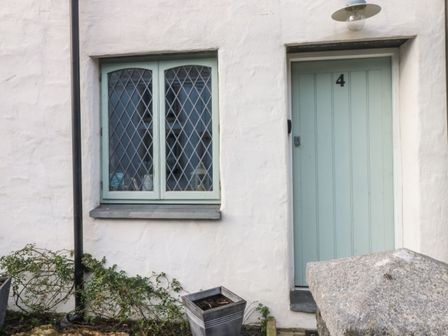 The exterior of a white building with a pale green door numbered 4 and a double window with diamond lattice panes