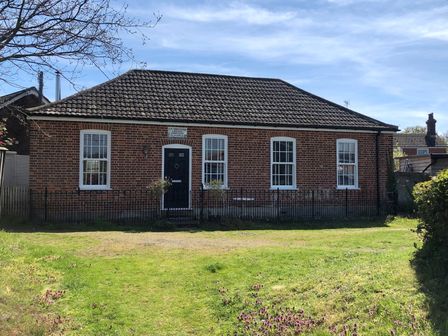 A single story brick building with four windows a black door and a tiled roof with a grassy yard in front at Ebenezer Chapel in Knodishall nr Saxmundham