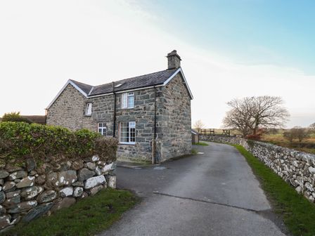 A stone house with a slate roof beside a paved road with stone walls and fields in the background at Ynys in Dyffryn Ardudwy