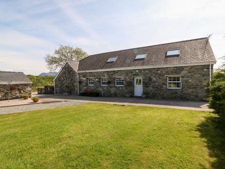 A stone cottage with a slate roof and skylights surrounded by grass at Bodrual Cottage in Rhosbodrual near Caernarfon